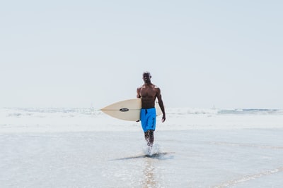 男子走在海滨,拿着白色的冲浪板
